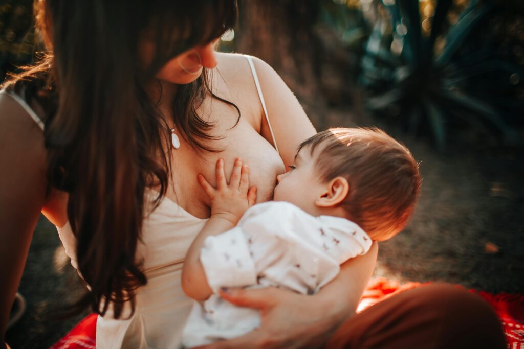 A tender moment of a mother breastfeeding her baby outdoors in natural light.