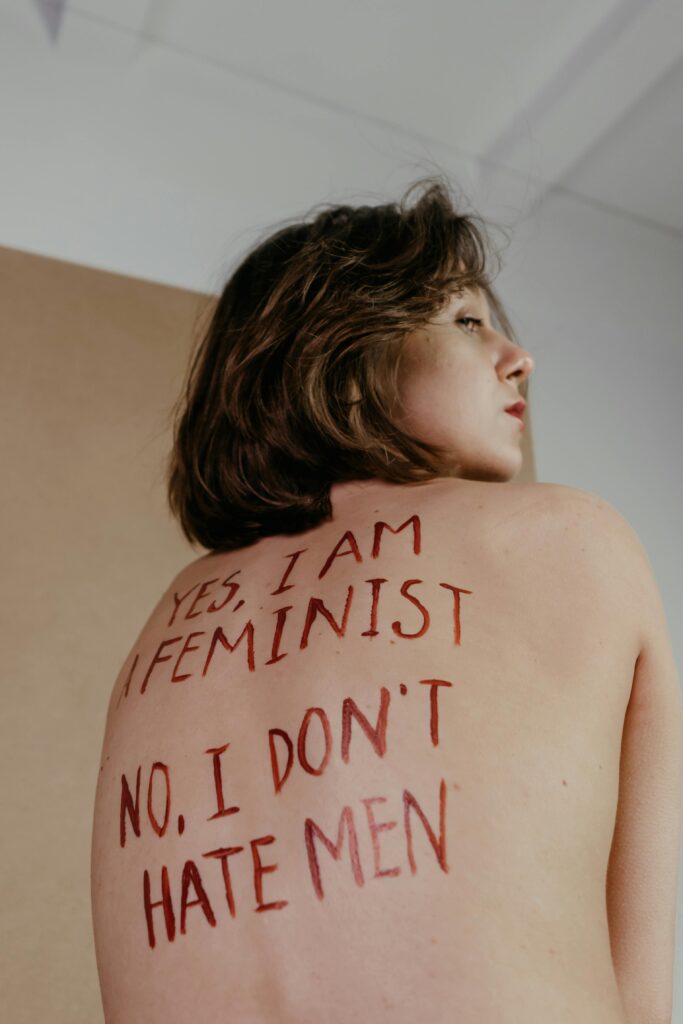 Portrait of a young woman with feminist message painted on her back, indoors.