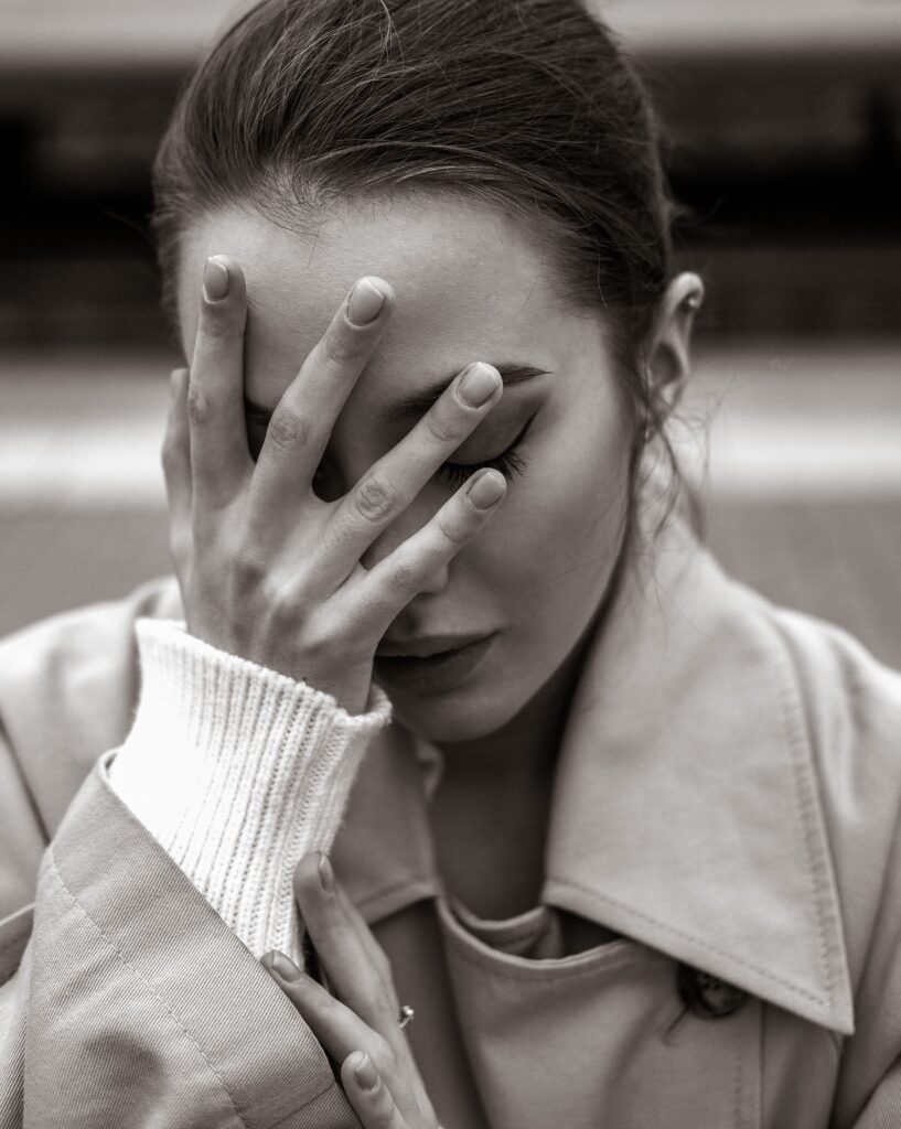 Artistic black and white portrait depicting emotion with a woman covering her face.